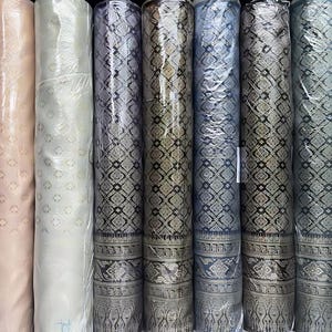 May include: Several rolls of fabric in a variety of colours, including white, pink, and patterned designs in grey and black. The rolls are wrapped in clear plastic, displaying the different textures and patterns.