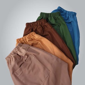 May include: An assortment of casual pants in various colors, including brown, tan, green, and blue. Each pair features an elastic waistband and a single pocket. The pants are made of a smooth, solid-colored fabric.