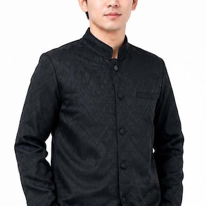 May include: Black long-sleeved shirt with a mandarin collar and a subtle geometric pattern. The shirt has a button-up front and a small pocket on the chest. The model is wearing the shirt with their hands in their pockets.