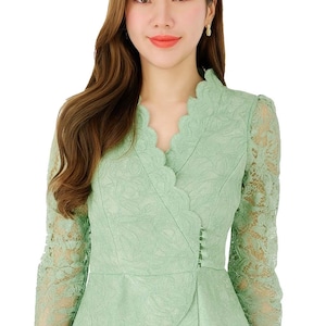 May include: A light green lace blouse with a scalloped neckline and long sleeves. The blouse has a wrap-style design with a peplum hem and button details. The intricate lace pattern adds a delicate touch to the garment.