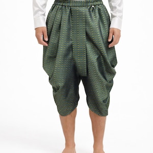 Op de afbeelding: Groen en goudkleurige shorts met een geplooide taille. De shorts zijn knielang en hebben een uniek, gedrapeerd ontwerp. De persoon draagt een wit shirt met lange mouwen.