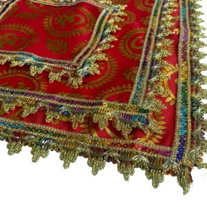 Può includere: Primo piano di un tessuto rosso con motivi paisley dorati. I bordi sono rifiniti con finiture decorative dorate e arcobaleno. Il tessuto appare a strati, con una forma quadrata visibile.