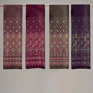 May include: Four rectangular textiles with intricate geometric patterns and ornate designs. The textiles are in shades of burgundy, magenta, and brown, with detailed patterns in pink, gold, and blue. The textiles are hanging from a wooden rod.