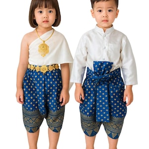 Könnte beinhalten: Zwei Kinder in traditioneller thailändischer Kleidung. Das Mädchen trägt ein weißes Oberteil und eine blaue Hose mit Muster, einen goldenen Gürtel und eine Halskette. Der Junge trägt ein weißes Hemd und eine blaue Hose mit Muster. Beide Outfits haben goldene Akzente.
