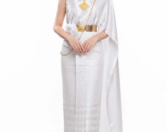 May include: A white, one-shoulder dress with gold accessories. The dress has a draped design and a patterned skirt. The model wears gold earrings, a necklace, and heels. The outfit is completed with a gold belt. The style is elegant and traditional.