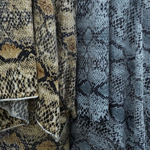 Op de afbeelding: Close-up van drie stoffen met een slangenprint. De stof aan de linkerkant is bruin, zwart en bruin. De middelste stof is bruin en bruin. De stof aan de rechterkant is grijs en zwart.