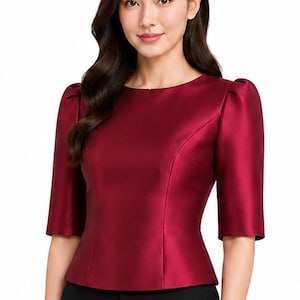 May include: A deep burgundy satin blouse featuring a round neckline, elbow-length sleeves with gathered puff shoulders, and a tailored bodice with vertical seam detailing that flares slightly at the waist, paired with black trousers.