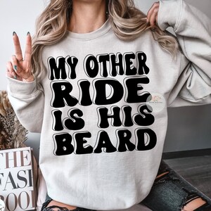 K&ouml;nnte beinhalten: Ein graues Sweatshirt mit dem Text "My Other Ride Is His Beard" in schwarzen umrandeten Buchstaben.