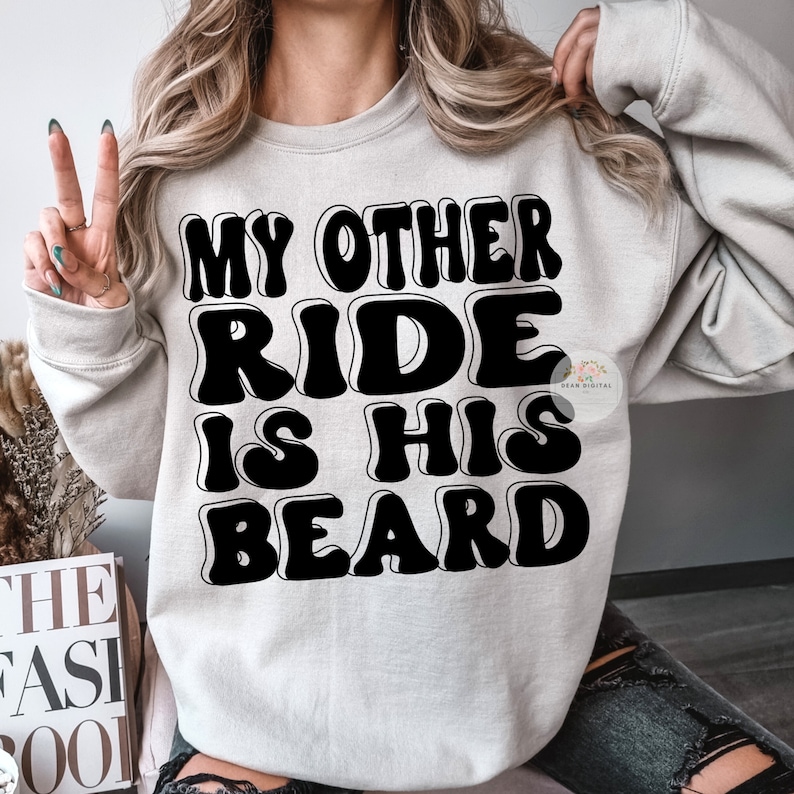 K&ouml;nnte beinhalten: Ein graues Sweatshirt mit dem Text "My Other Ride Is His Beard" in schwarzen umrandeten Buchstaben.