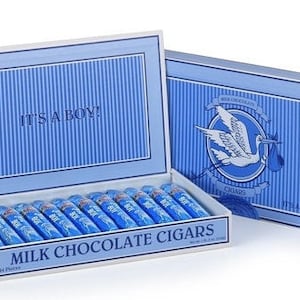 May include: A blue and white box with the words "It's a Boy!" on the lid. The box contains milk chocolate cigars. The box is decorated with a stork carrying a baby.
