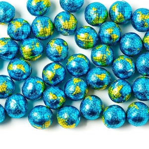 May include: A collection of globe-shaped candies wrapped in blue and yellow foil. The foil-wrapped candies are scattered across a white surface. The blue foil represents the oceans, and the yellow foil represents the continents.