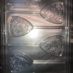 Peut inclure: Un moule en plastique transparent pour faire quatre bonbons en forme de sucette. Chaque pièce présente un design détaillé d'un emblème de pompiers avec les mots "Fire Department" et "New York City" dans un design circulaire. Le moule a quatre bâtonnets pour tenir les sucettes.