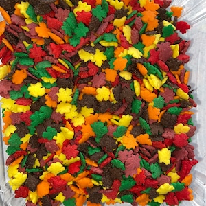 May include: A container of colorful fall leaf sprinkles. The sprinkles are in various shades of red, orange, yellow, green, and brown. They are shaped like leaves and are perfect for decorating cakes, cupcakes, and other desserts.