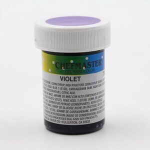 Peut inclure: Un petit pot rond de colorant alimentaire en gel violet. Le pot a un couvercle blanc et une étiquette qui indique "Chefmaster Gel Base Color Violet". L'étiquette comprend également une liste d'ingrédients et d'autres informations.
