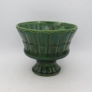 Puede incluir: Un cuenco con pedestal de cerámica verde con un borde festoneado y un exterior acanalado texturizado. El cuenco se asienta sobre una base de pedestal decorativa corta. El acabado brillante le da al cuenco un aspecto vintage.