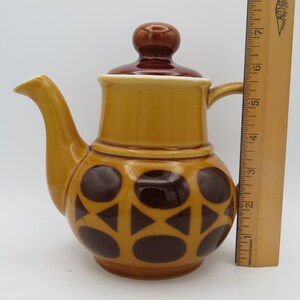 May include: A brown and yellow ceramic teapot with a brown lid and a geometric pattern of brown circles and triangles. The teapot is about 6 inches tall.