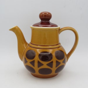 May include: A brown and yellow ceramic teapot with a brown lid and a geometric pattern of brown circles and triangles.