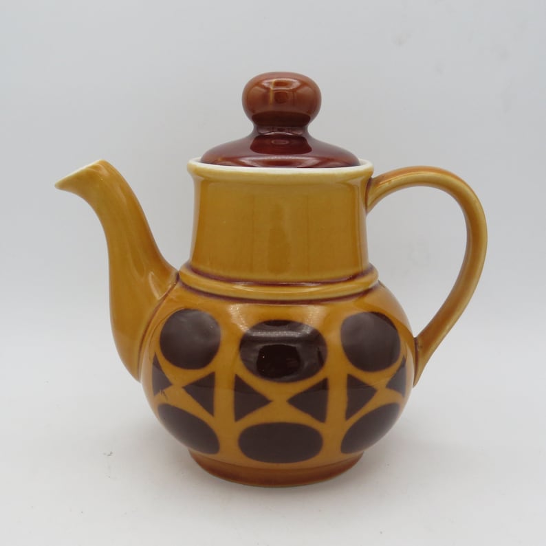 May include: A brown and yellow ceramic teapot with a brown lid and a geometric pattern of brown circles and triangles.