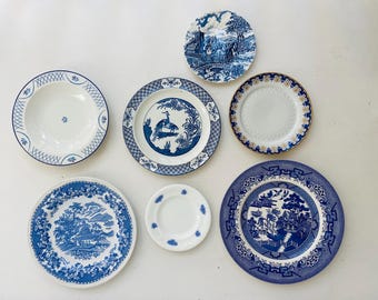 May include: A collection of six ceramic plates featuring various designs. One plate displays a blue and white landscape, another a bird motif, one has a gold rim, one a blue floral pattern, one a small white plate, and one a blue willow pattern.