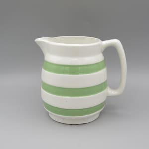 Puede incluir: Una taza de cerámica blanca con un asa negra y el texto "But first, coffee" en negro, con una fuente de estilo manuscrito. La taza está sobre una superficie blanca.