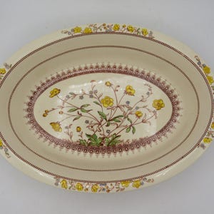 May include: Oval cream-coloured serving platter with a floral design. The centre features a bouquet of yellow flowers and green leaves, framed by a burgundy and cream border. The rim is decorated with yellow floral accents and burgundy trim.