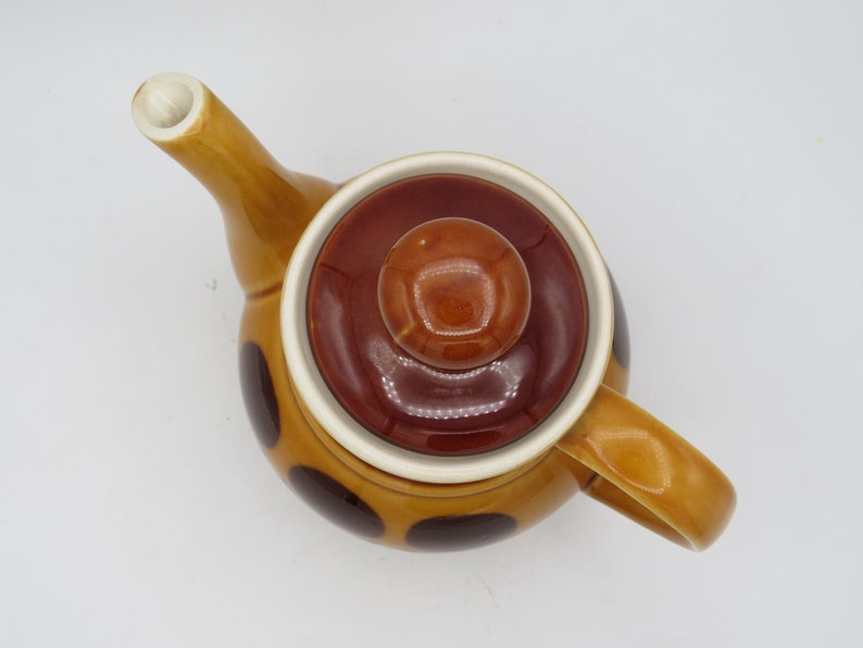 May include: A brown and yellow teapot with a brown lid and a brown knob. The teapot has a polka dot pattern in brown.