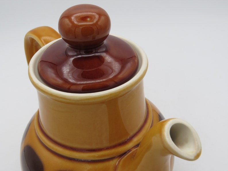 May include: A brown and tan ceramic teapot with a brown lid and a brown handle. The teapot has a brown and white pattern on the body.
