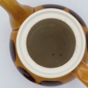 May include: A brown and white ceramic teapot with a lid and a handle. The teapot has a polka dot pattern with brown dots on a white background.