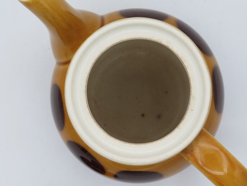 May include: A brown and white ceramic teapot with a lid and a handle. The teapot has a polka dot pattern with brown dots on a white background.