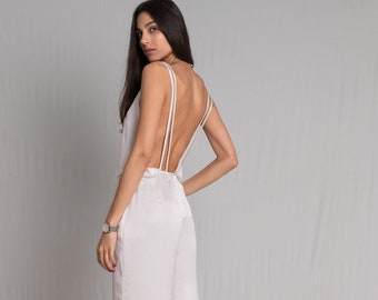 White satin jumpsuit with a cowl neckline, thin straps, front pockets and a risque low back