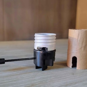 May include: A black and silver lamp socket with a black switch and a cardboard tube. The lamp socket has a silver threaded top and a black base with three legs. The switch is attached to the base.