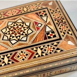 May include: A wooden box with intricate geometric patterns inlaid in various shades of brown, red, and black. The box is made using the art of marquetry, a technique of inlaying different woods to create a design.