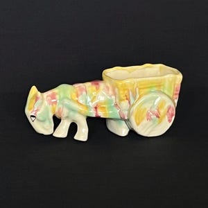May include: A colourful ceramic planter shaped like a donkey pulling a wagon. The planter is painted in shades of green, yellow, pink, and blue.