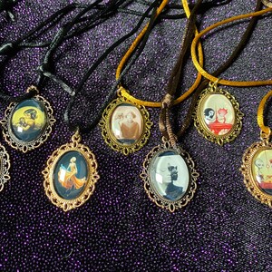 May include: Seven gold-tone oval pendant necklaces with black and brown cords. Each pendant features a different vintage-style illustration under a glass dome.