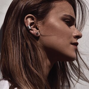 May include: A woman with long brown hair wearing a silver ear cuff and a small silver stud earring.