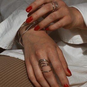 A hand with red nail polish displaying silver spiral rings, leaning against a knee covered in a white cloth