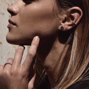 May include: A close-up of a woman's face with a silver stud earring and a silver ear cuff in her left ear. She is wearing a ring on her right ring finger.
