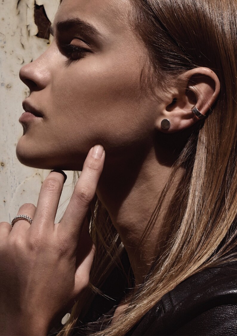 May include: A close-up of a woman's face with a silver stud earring and a silver ear cuff in her left ear. She is wearing a ring on her right ring finger.