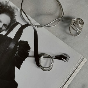 A stylized black and white photo featuring a hand with silver rings and a bracelet, laying over an open magazine with artistic imagery.