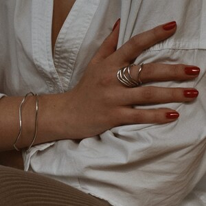 Hand with red nail polish showing silver spiral rings, resting on a white cloth with a relaxed, elegant posture.