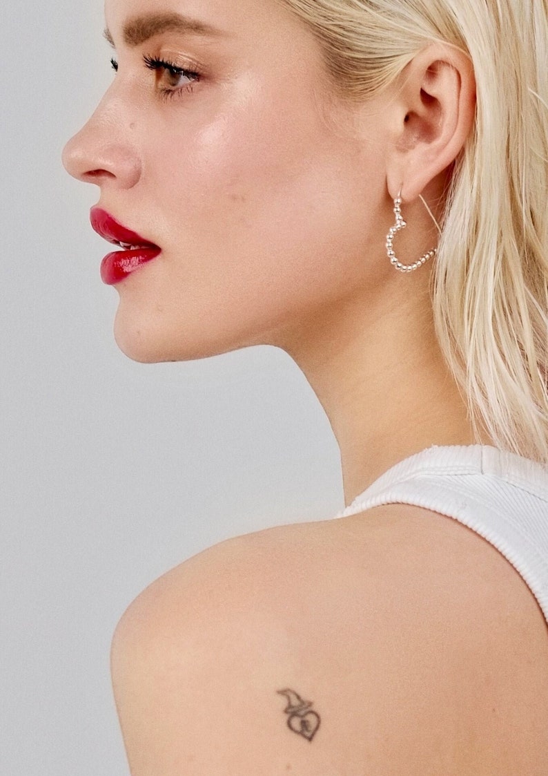 Stylish lady with a shoulder tattoo showcasing her Statement Silver Heart Hoop Earrings.