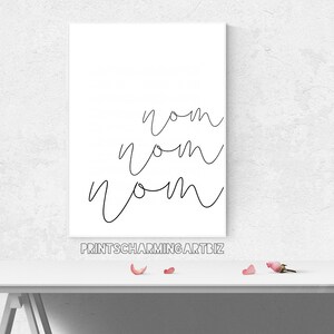 K&ouml;nnte beinhalten: Ein wei&szlig;es Poster mit dem Wort "nom" dreimal in schwarzer Kursivschrift geschrieben. Das Poster befindet sich auf einem wei&szlig;en Tisch mit rosafarbenen Bl&uuml;tenbl&auml;ttern, die auf der Oberfl&auml;che verstreut sind. Der Text "printscharmingart.biz" ist in Schwarz am unteren Rand des Posters gedruckt.