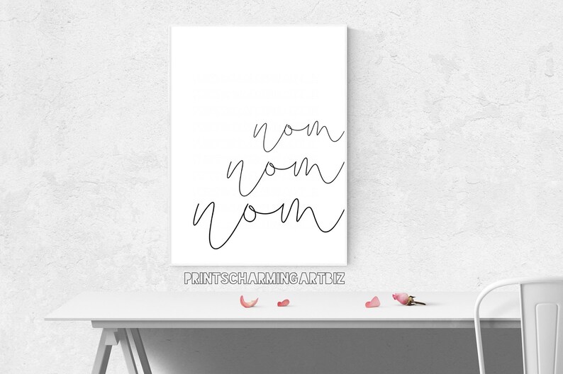 K&ouml;nnte beinhalten: Ein wei&szlig;es Poster mit dem Wort "nom" dreimal in schwarzer Kursivschrift geschrieben. Das Poster befindet sich auf einem wei&szlig;en Tisch mit rosafarbenen Bl&uuml;tenbl&auml;ttern, die auf der Oberfl&auml;che verstreut sind. Der Text "printscharmingart.biz" ist in Schwarz am unteren Rand des Posters gedruckt.