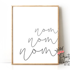 K&ouml;nnte beinhalten: Ein schwarz-wei&szlig;er druckbarer Wandkunstdruck mit dem Wort "nom", das dreimal in einer kursiven Schrift geschrieben ist. Der Druck ist in einem hellbraunen Holzrahmen gerahmt.