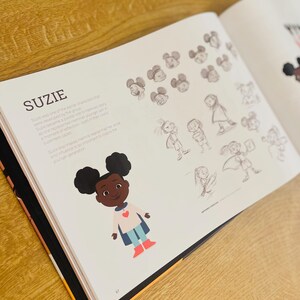 May include: Illustration of a young girl with brown skin and curly black hair wearing a blue cape and red boots. She is smiling and has a red heart on her shirt. The text "Suzie" is written in black above the illustration.