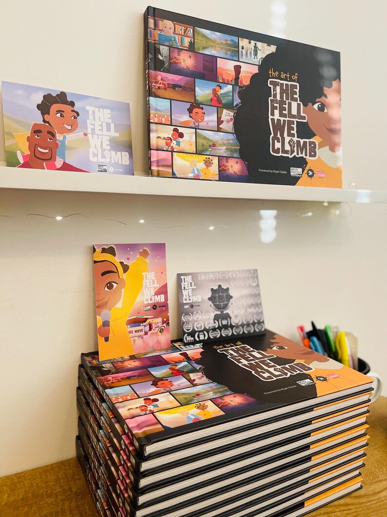 May include: A stack of 12 black and orange hardback books with the title "The Fell We Climb" on the top book. The book cover features a collage of colourful illustrations. There is a smaller book with the same title and a bookmark with a cartoon character on it.