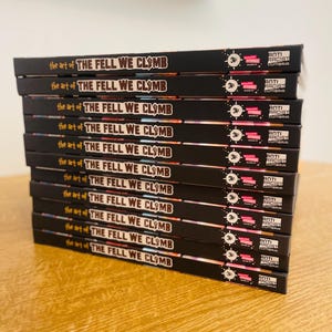 May include: A stack of 10 black books with the title "The Fell We Climb" and the words "the art of" printed on each book. Each book has a sticker on the spine that says "Anti-Racist Cumbria" and a number "34" printed on the sticker.