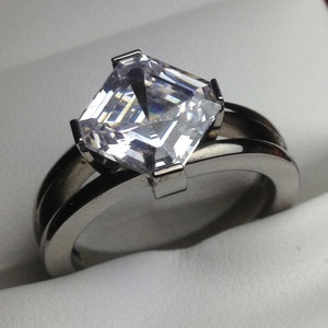 May include: A silver ring with a large, clear, square-shaped gemstone.