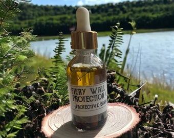May include: A clear glass bottle with a gold-coloured dropper top, filled with a yellow liquid and botanical elements. The label reads "Fiery Wall Protection Oil" with "Protective Barrier" below. The bottle sits on a small wooden slice, with a natural outdoor background.