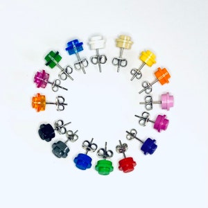 Könnte beinhalten: Ein Set mit 16 bunten Lego-Stein-Ohrringen. Die Ohrringe sind aus Kunststoff und haben einen silbernen Stift. Die Farben der Ohrringe umfassen Rot, Orange, Gelb, Grün, Blau, Lila, Rosa, Weiß, Schwarz und Grau.